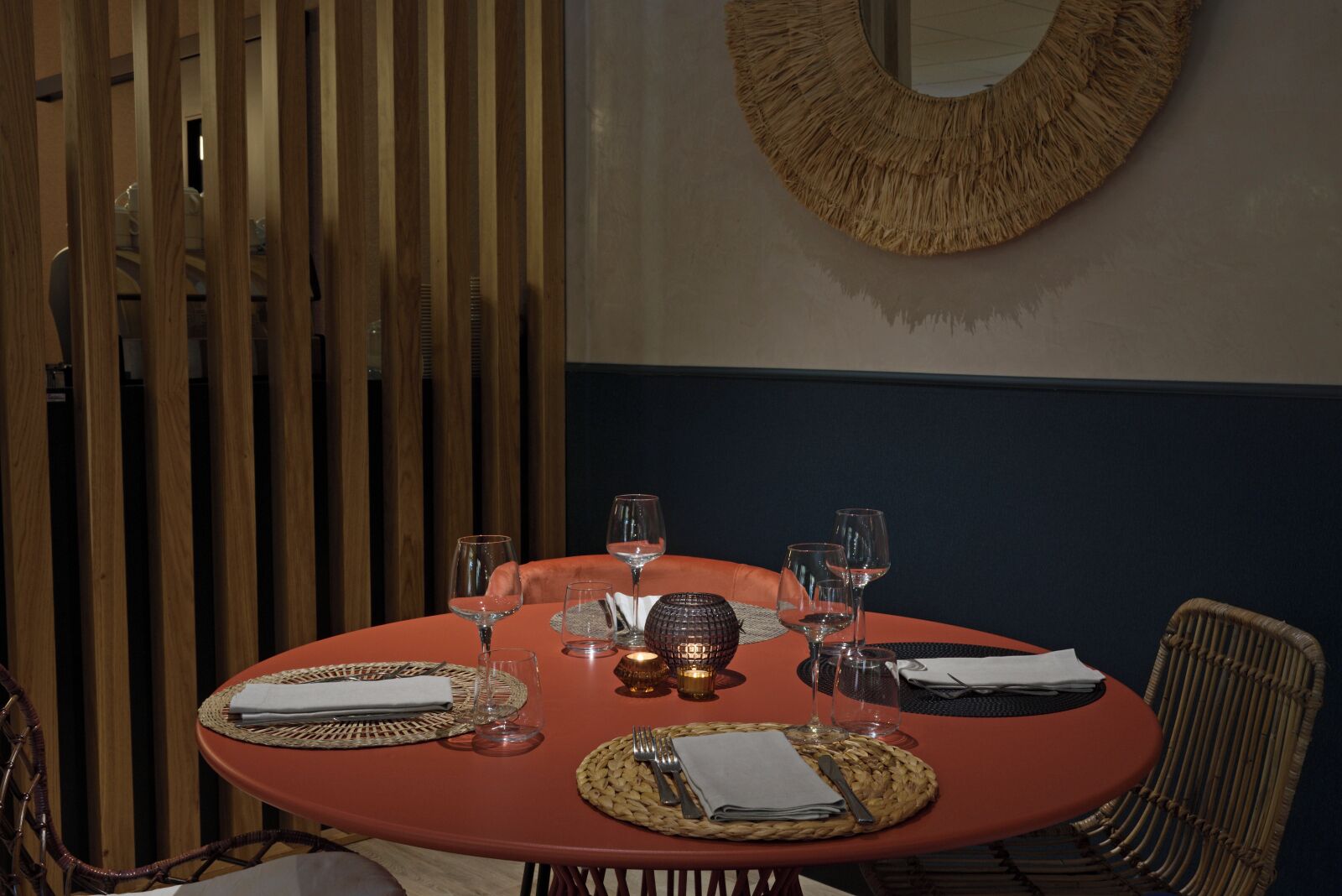 A round table set for dining with woven placemats, wine glasses, and a decorative centerpiece.