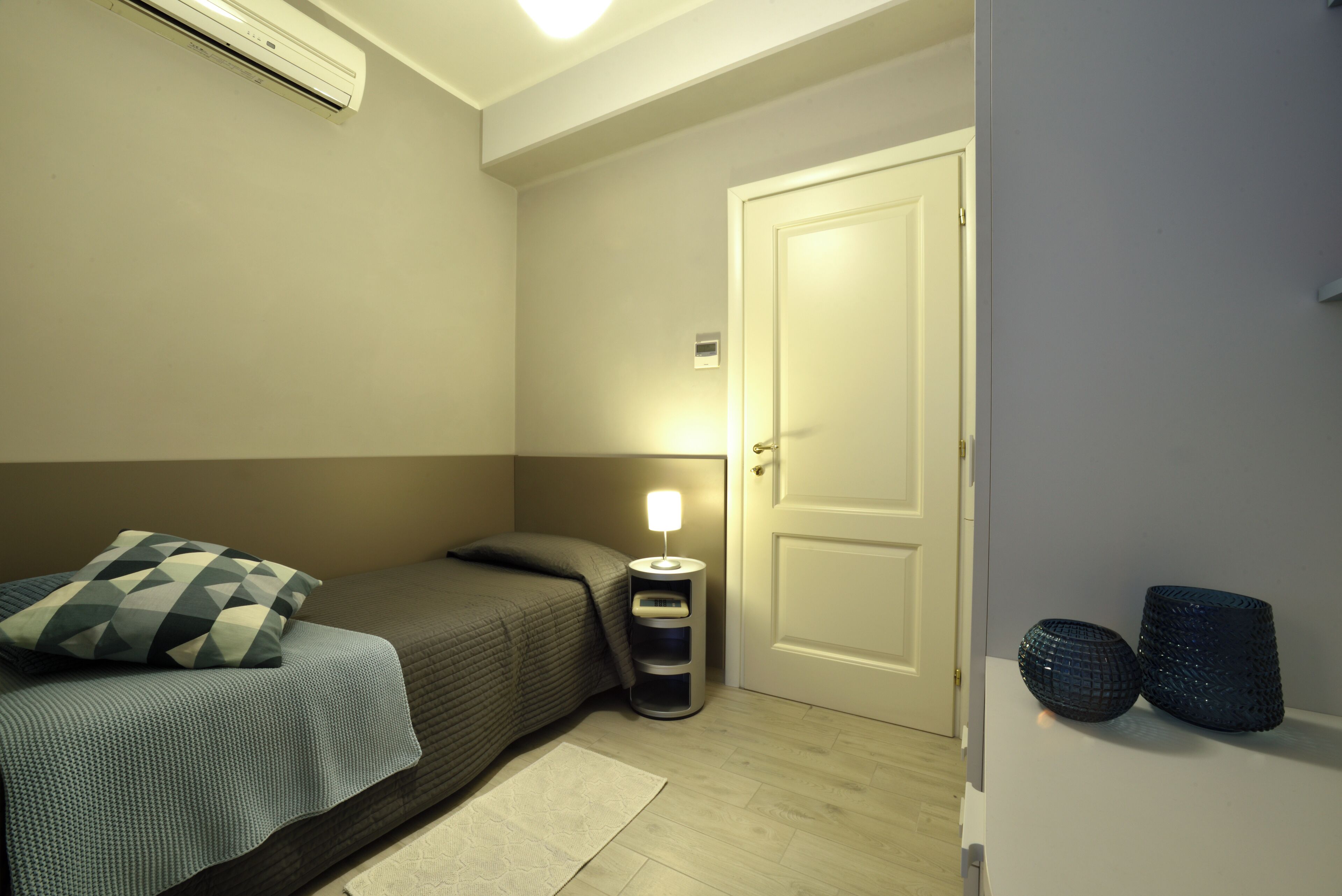 Un dormitorio pequeño y ordenado con cama, lámpara de noche y una puerta.