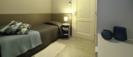 Un dormitorio pequeño y ordenado con cama, lámpara de noche y una puerta.