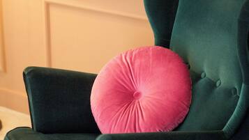 A green armchair with a pink cushion in a room with a bookshelf in the background.