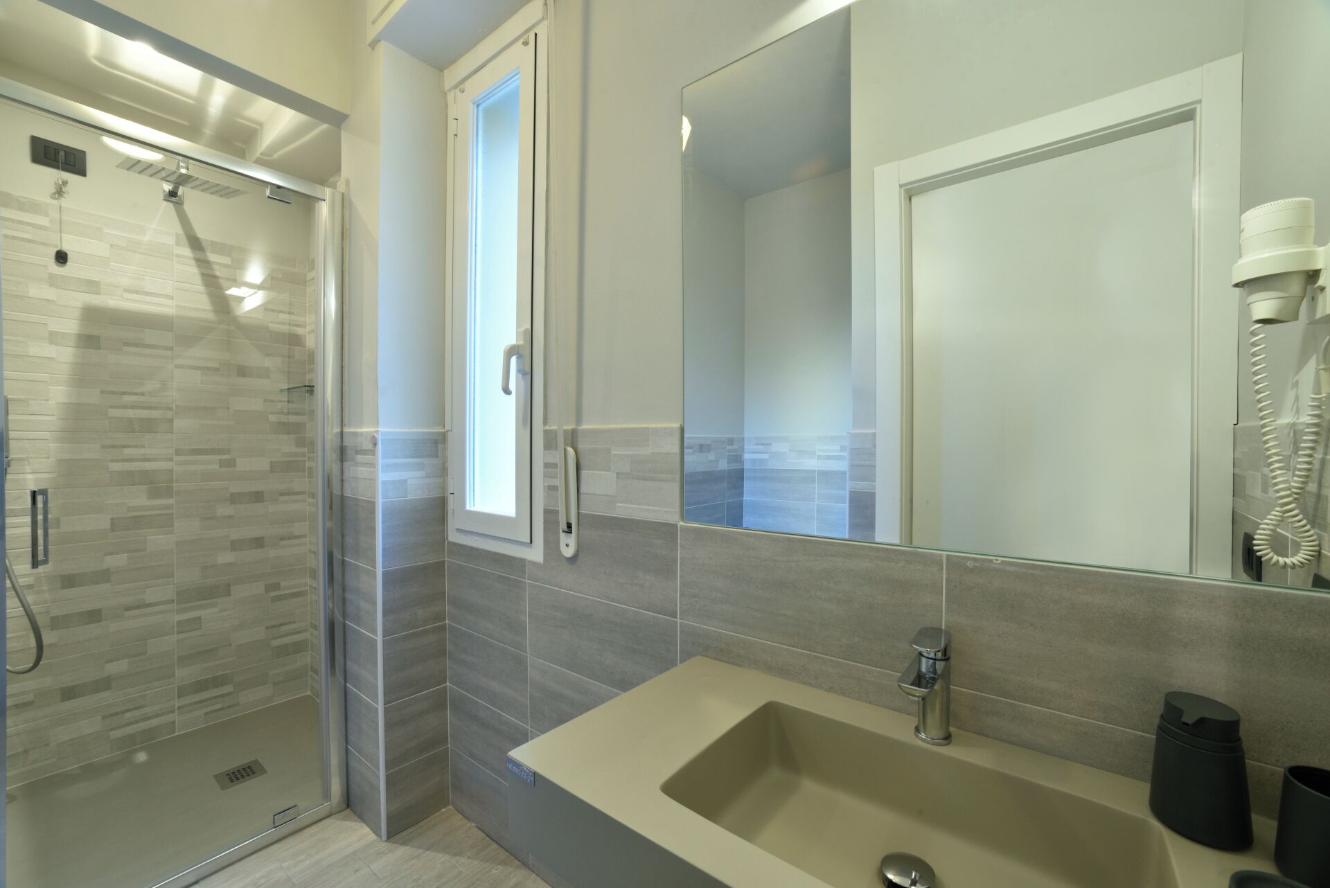 A modern bathroom with a glass shower enclosure, a large mirror, and a beige sink.