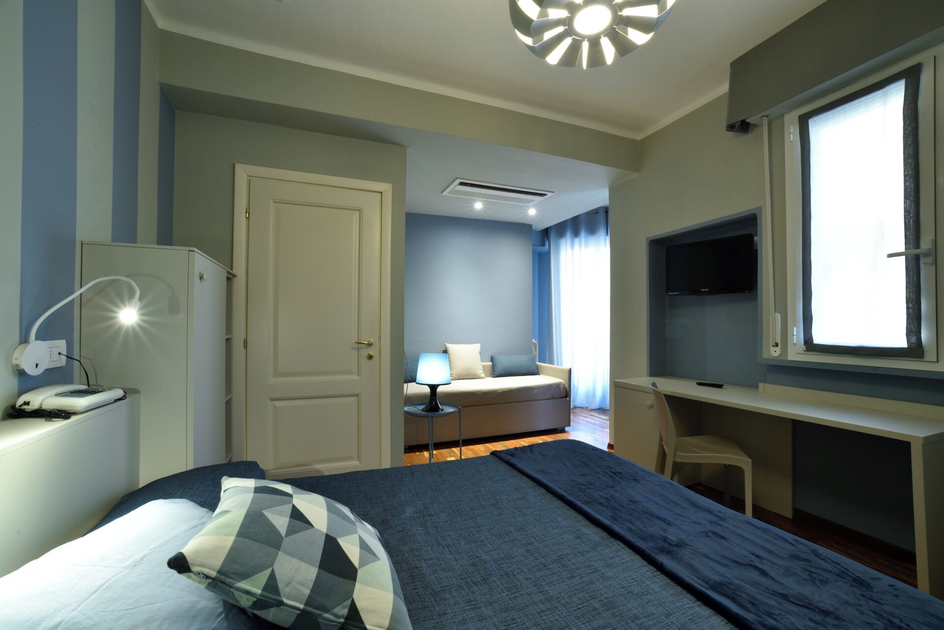 Una habitación de hotel con una cama, un escritorio, un televisor y una ventana.