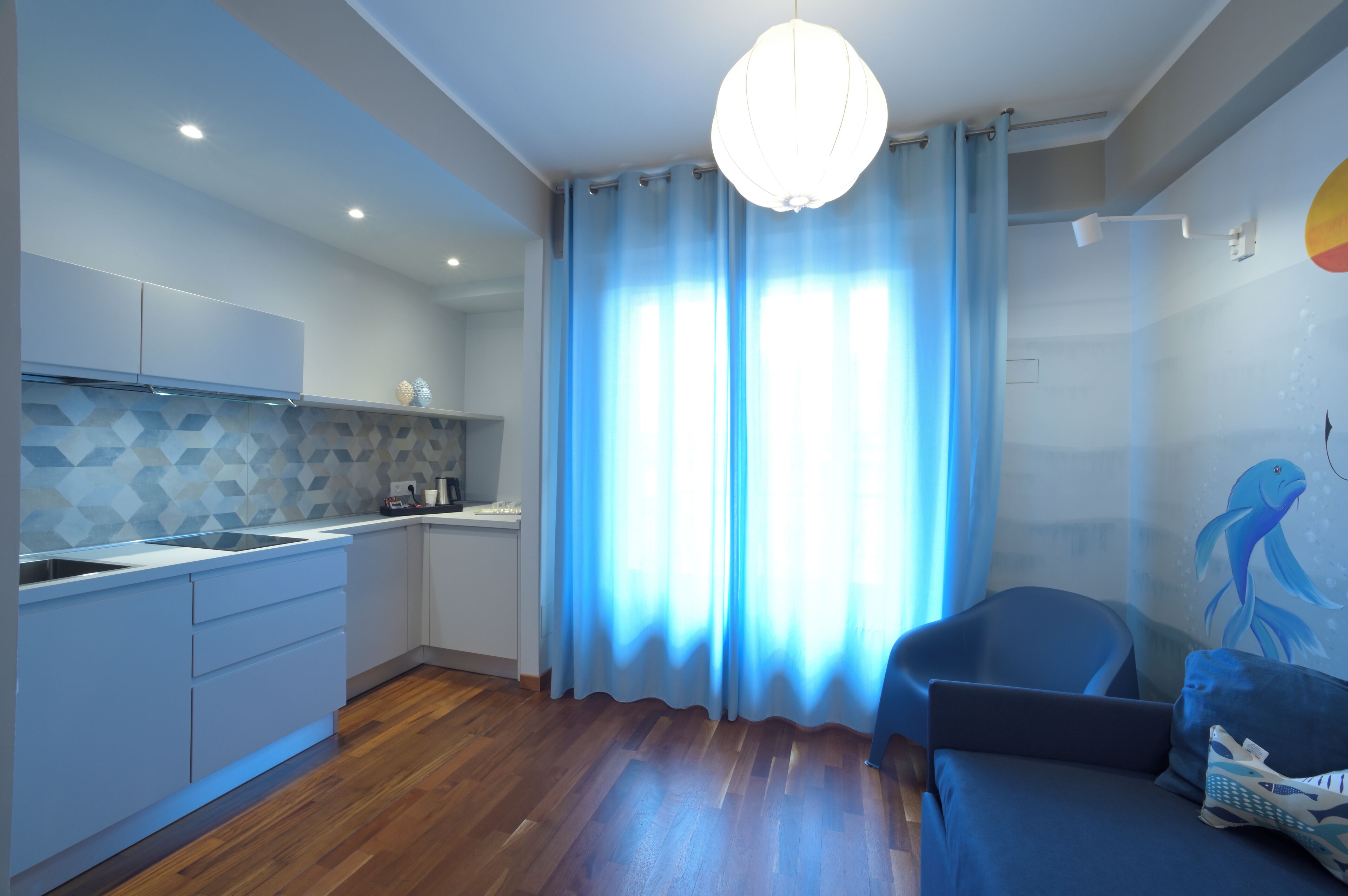 Eine moderne Küche mit geometrischer Spritzschutz, ein Essbereich mit blauem Sofa und ein großes Fenster mit blauen Vorhängen.