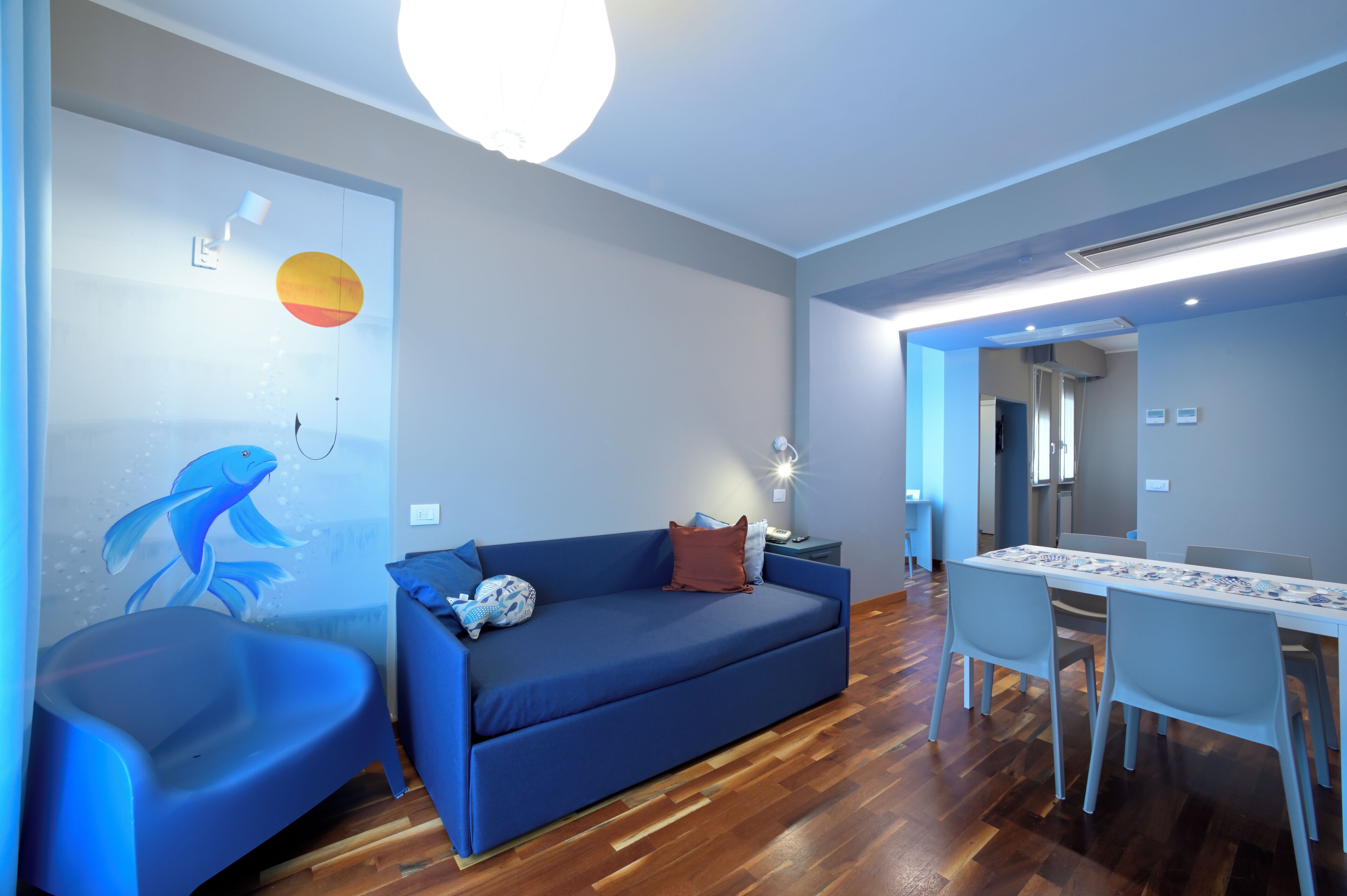 Un salon moderne avec un canapé bleu, une table à manger et des chaises, ainsi qu’une fresque murale.