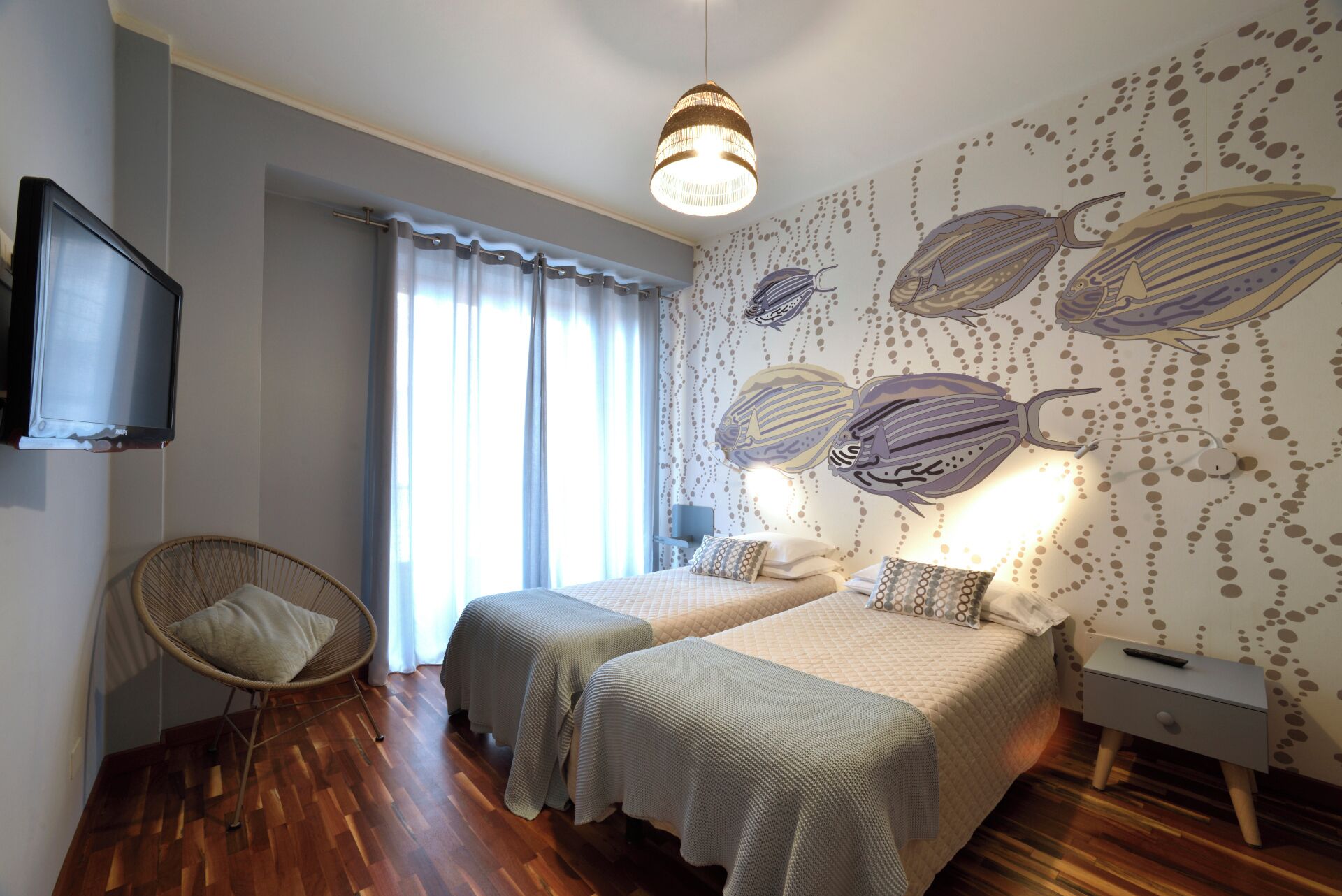 Una camera da letto con due letti, una televisione, una poltrona in vimini e un muro decorato con un murale a tema pesce.