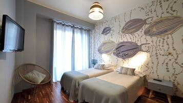 Una camera da letto con due letti, una televisione, una poltrona in vimini e un muro decorato con un murale a tema pesce.