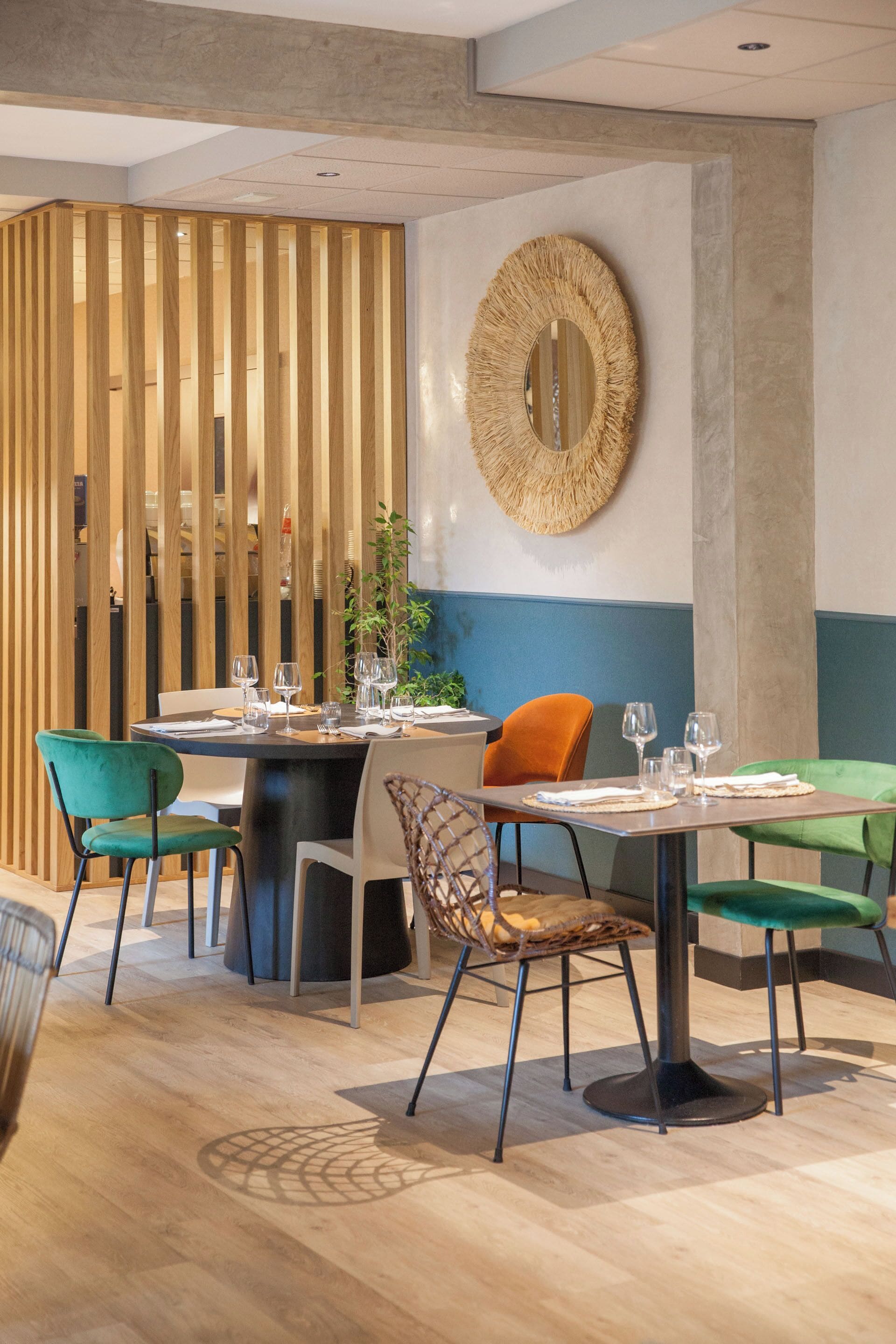 Un comedor moderno con separadores de madera, un espejo redondo y sillas verdes y naranjas.