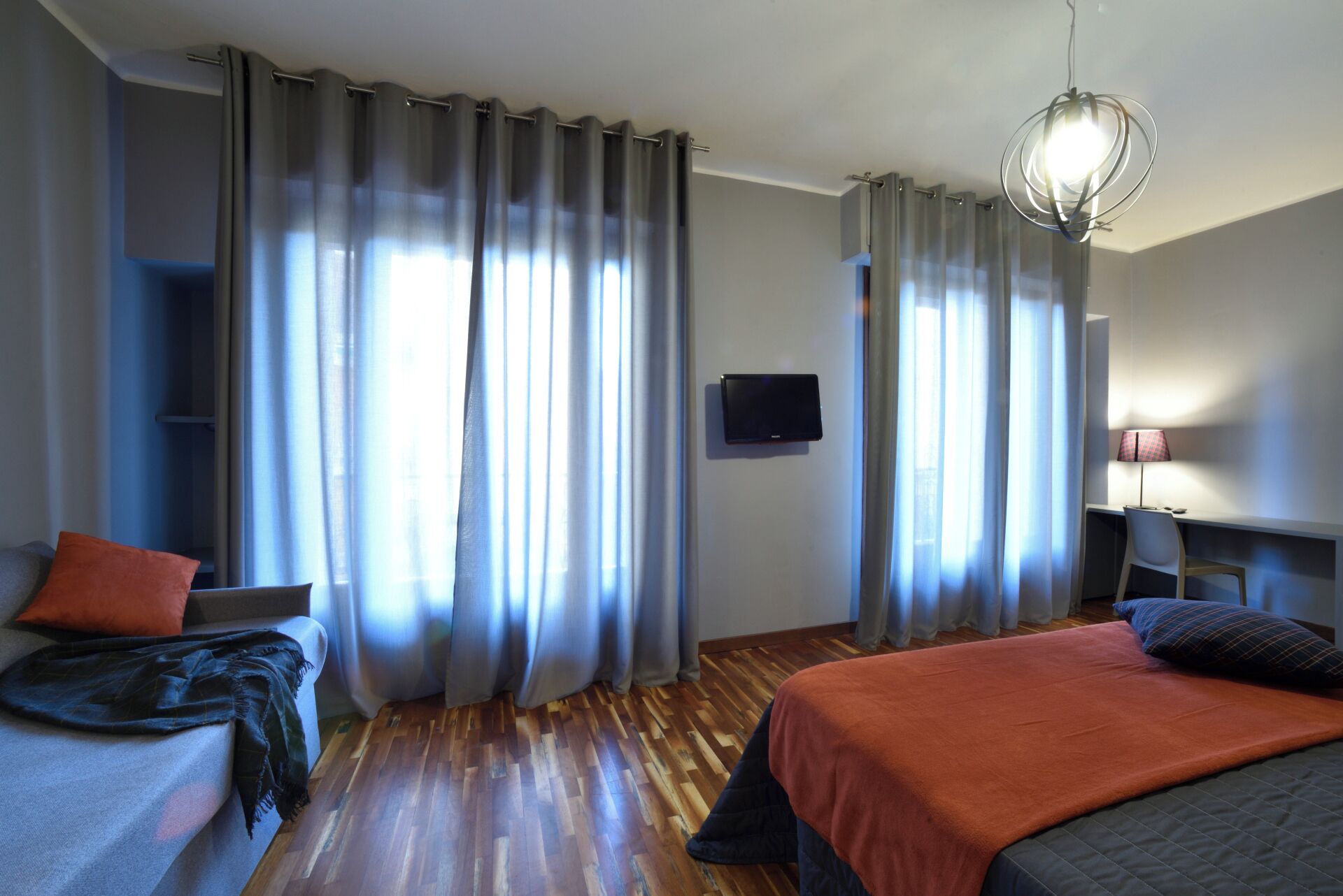 A hotel room with a bed, a desk, a TV, and curtains.