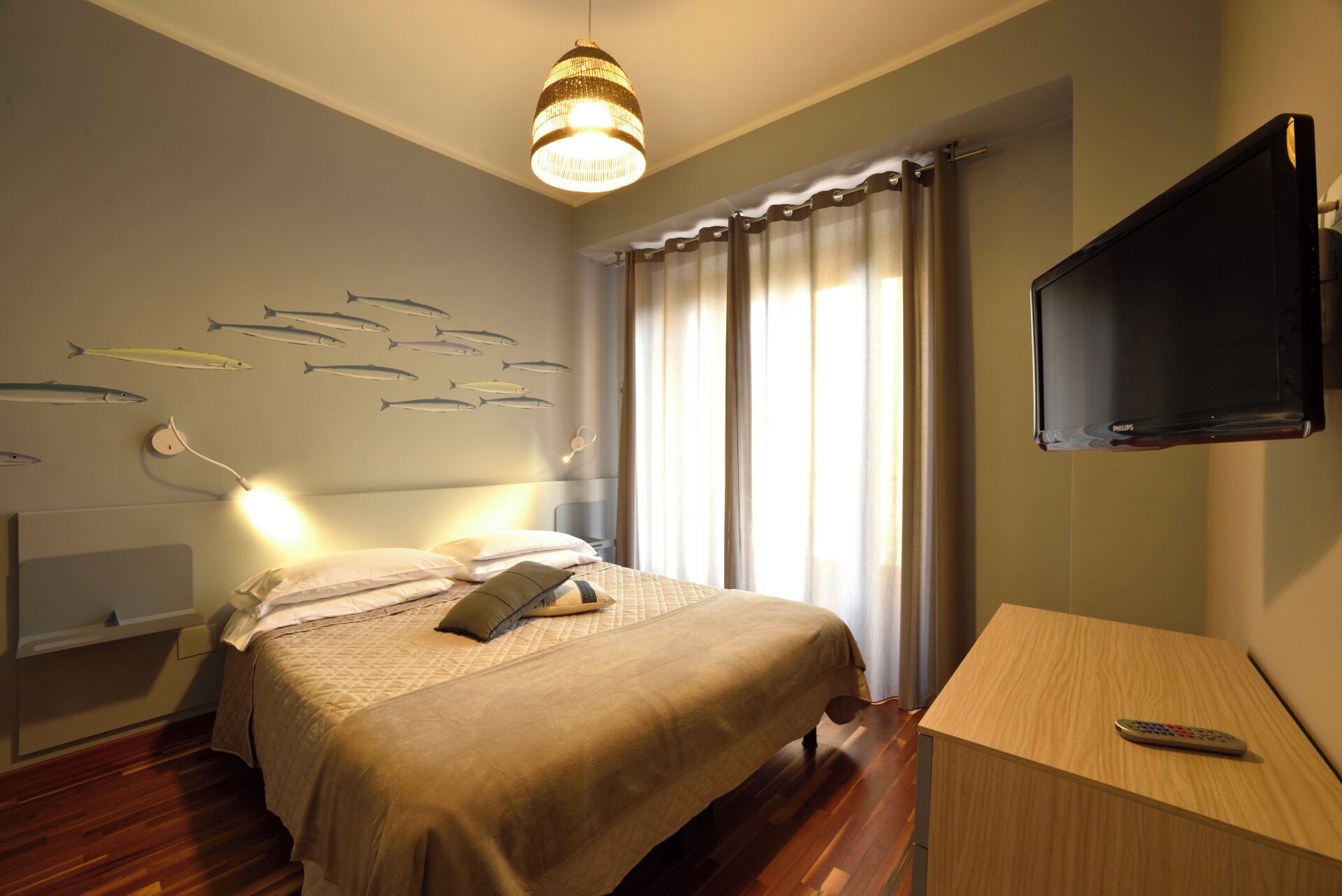 A hotel room with a bed, a TV, a desk, and a wall with fish decals.