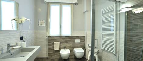 Un baño moderno con un lavamanos grande, bidé y cabina de ducha de vidrio.