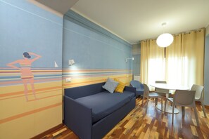 A room with a blue sofa, a small table with chairs, and a mural on the wall. - Hotel Bristol (Alassio)