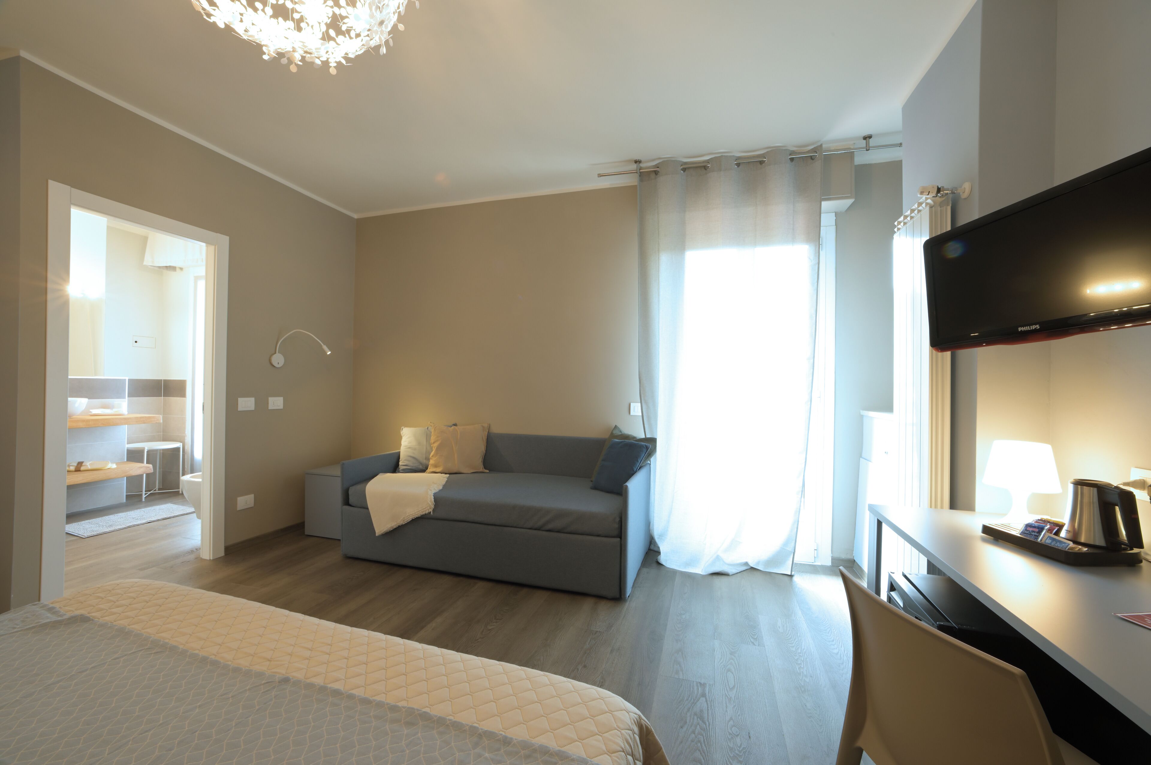 Une chambre d’hôtel moderne équipée d’un lit, d’un canapé, d’un bureau avec une lampe et d’une télévision.