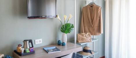 Una habitación moderna con un escritorio de madera, una silla, un televisor montado en la pared, un perchero con abrigo y un florero con flores.