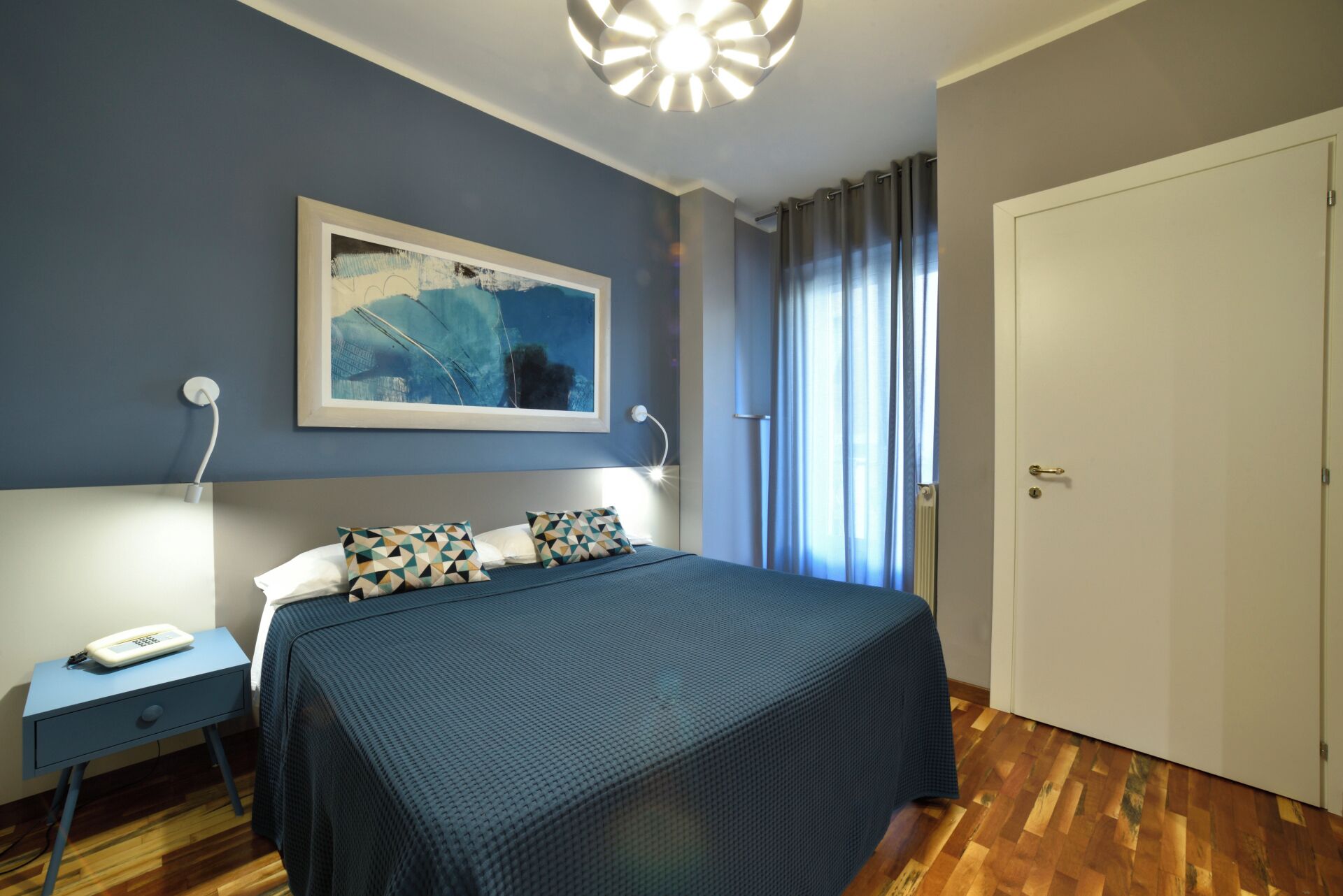 A bedroom with a bed, a nightstand, a telephone, and a door.