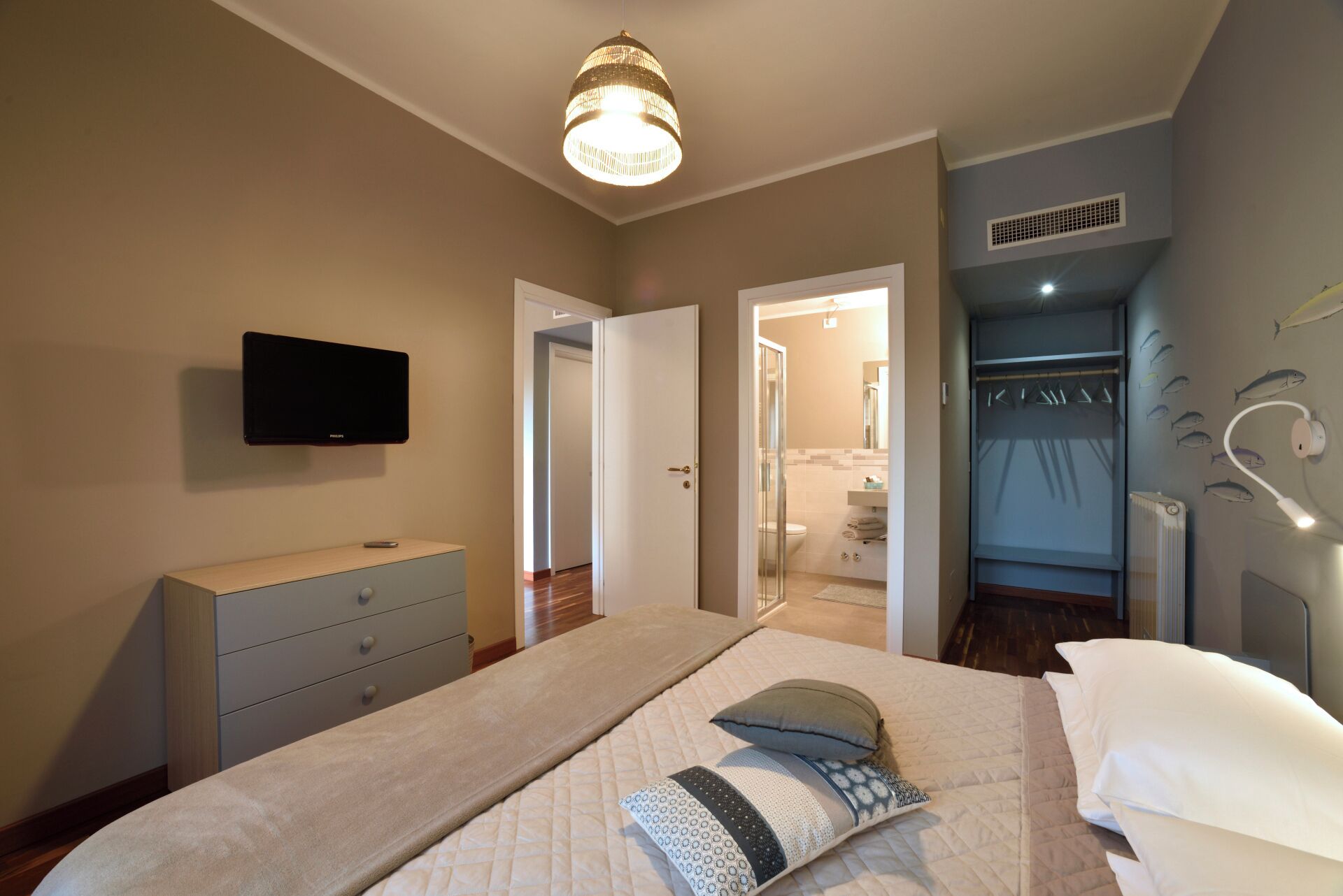 Une chambre à coucher avec un lit, une télévision, une armoire et une salle de bain visible à travers une porte ouverte.