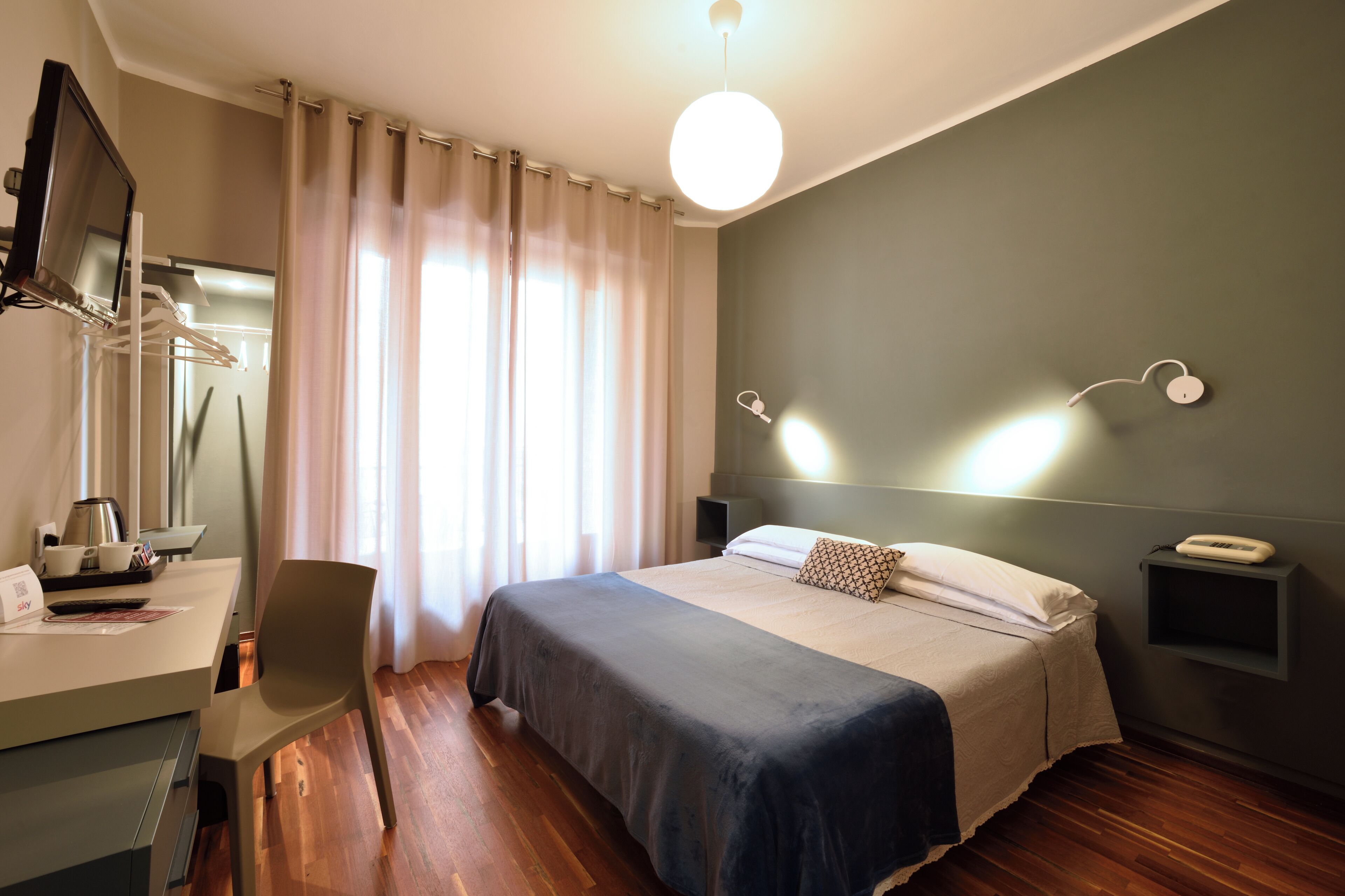 Ein modernes Hotelzimmer mit Bett, Schreibtisch, Stuhl, Fernseher und Nachttisch.