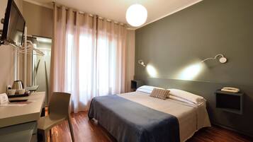 Ein modernes Hotelzimmer mit Bett, Schreibtisch, Stuhl, Fernseher und Nachttisch.