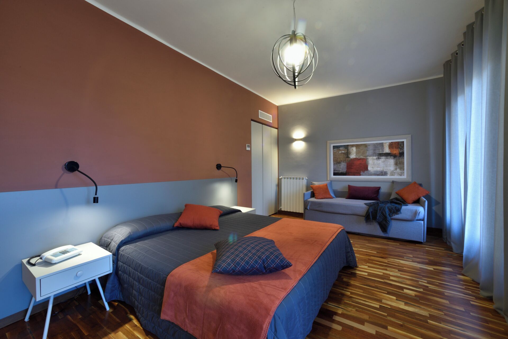 A modern bedroom with a large bed, bedside table, and a sofa in the background.