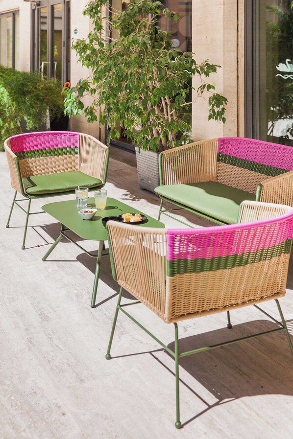 A patio area with wicker furniture and a table set with a bowl of fruit and drinks. - Hotel Bristol (Alassio)