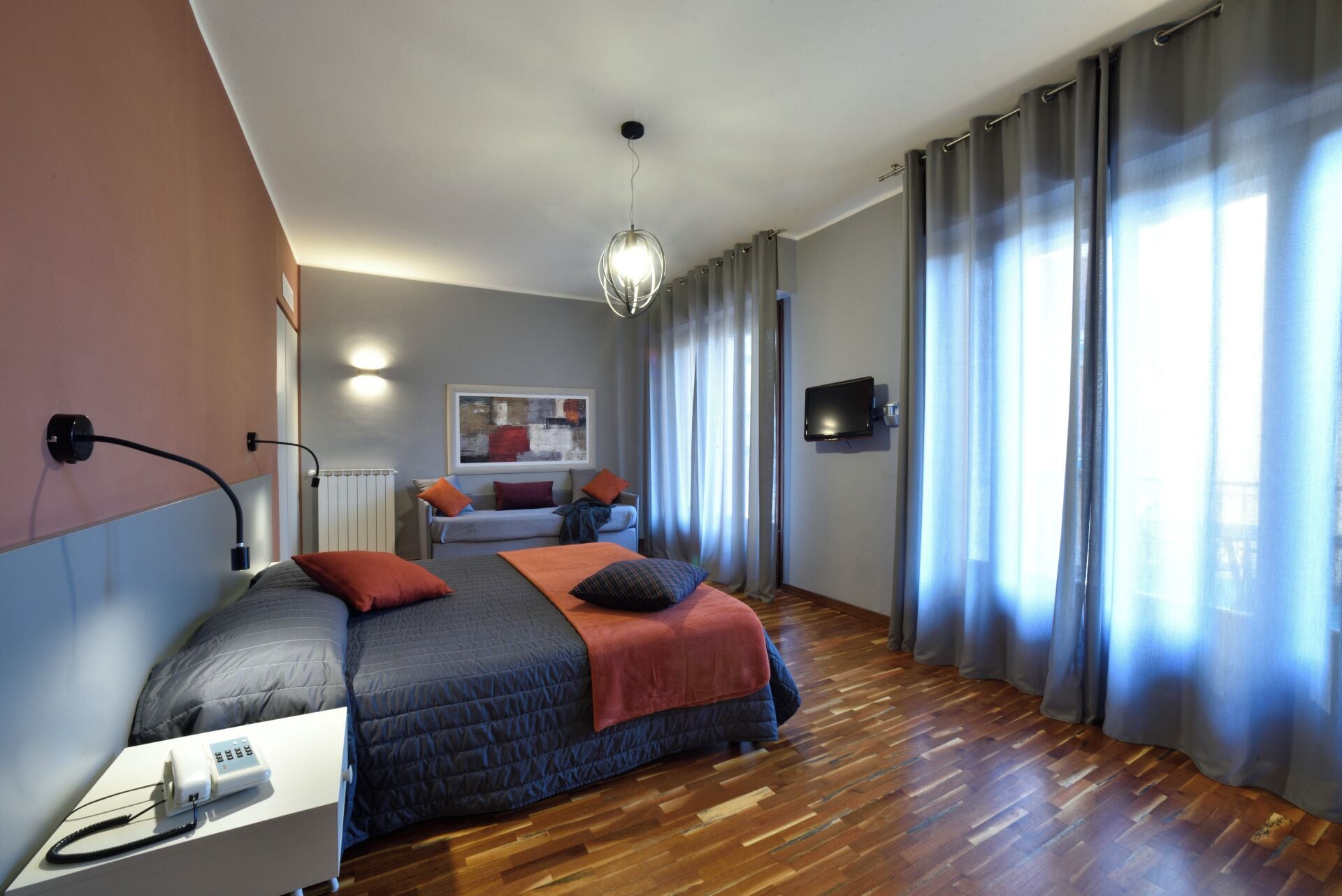 Un dormitorio moderno con cama, escritorio, lámpara, televisor y un cuadro en la pared.