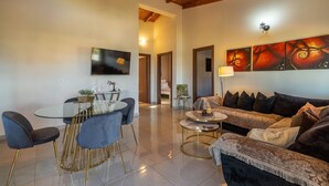 A modern living room with a round glass table, two sofas, a TV mounted on the wall, and a painting above the sofa.