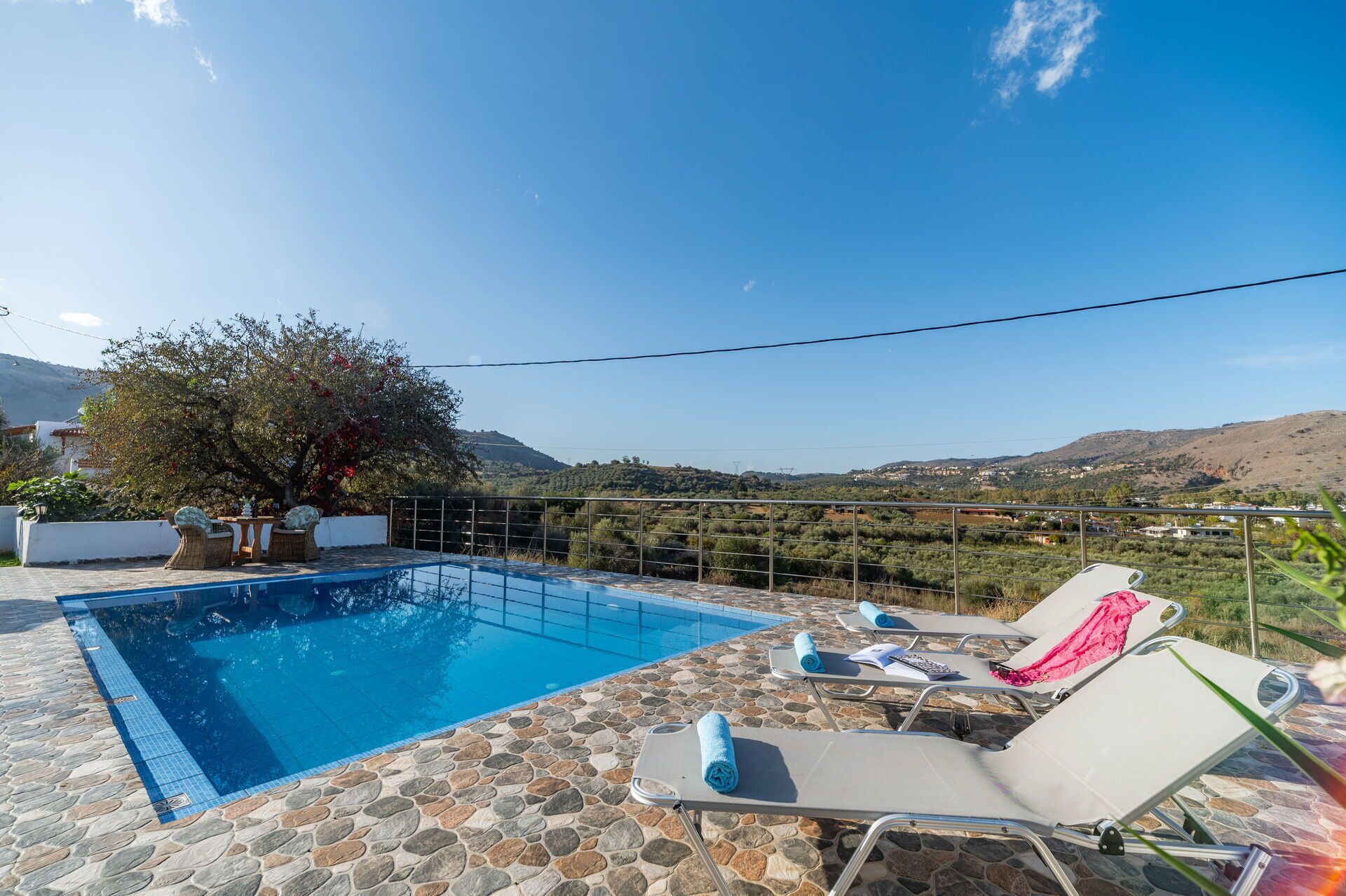 A pool area with stone flooring, lounge chairs, and a view of hills.