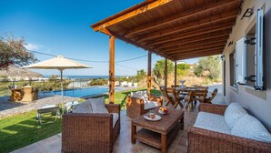 A covered patio with wicker furniture, a pool, and a view of the sea.