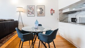 Eine moderne Küche mit Mikrowelle, einem Glastisch mit Stühlen, einer Couch und zwei gerahmten Kunstwerken an der Wand.