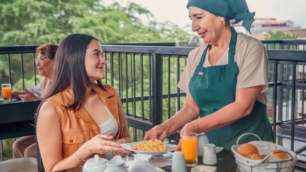 A person serving food at a table with a sign that reads "DI COSTA". - Di Costa Hoteles (Piura)