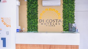A reception desk with a wooden base and a glass top, flanked by two vertical green plant walls. - Di Costa Hoteles (Piura)