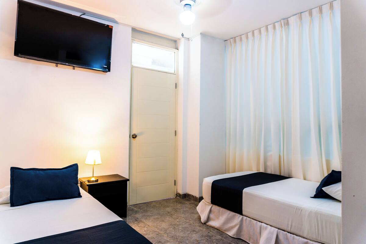 Une chambre d’hôtel avec deux lits, un téléviseur fixé au mur, une lampe de chevet et une porte.