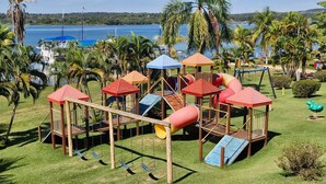A playground with slides and swings, surrounded by palm trees and a view of a lake. - Náutico Flat: Perfect Getaway in Caldas Novas (Caldas Novas)