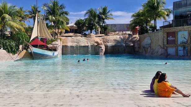 A swimming pool with clear water, a sailboat, palm trees, and a rocky backdrop. - Náutico Flat: Perfect Getaway in Caldas Novas (Caldas Novas)