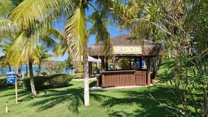 A beachside hut with a thatched roof, surrounded by lush greenery and palm trees. - Náutico Flat: Perfect Getaway in Caldas Novas (Caldas Novas)
