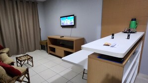 A living room with a sofa, a television, a small wooden table, and a white counter. - Náutico Flat: Perfect Getaway in Caldas Novas (Caldas Novas)