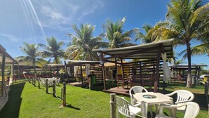 An outdoor seating area with tables and chairs, surrounded by palm trees and covered structures. - Náutico Flat: Perfect Getaway in Caldas Novas (Caldas Novas)