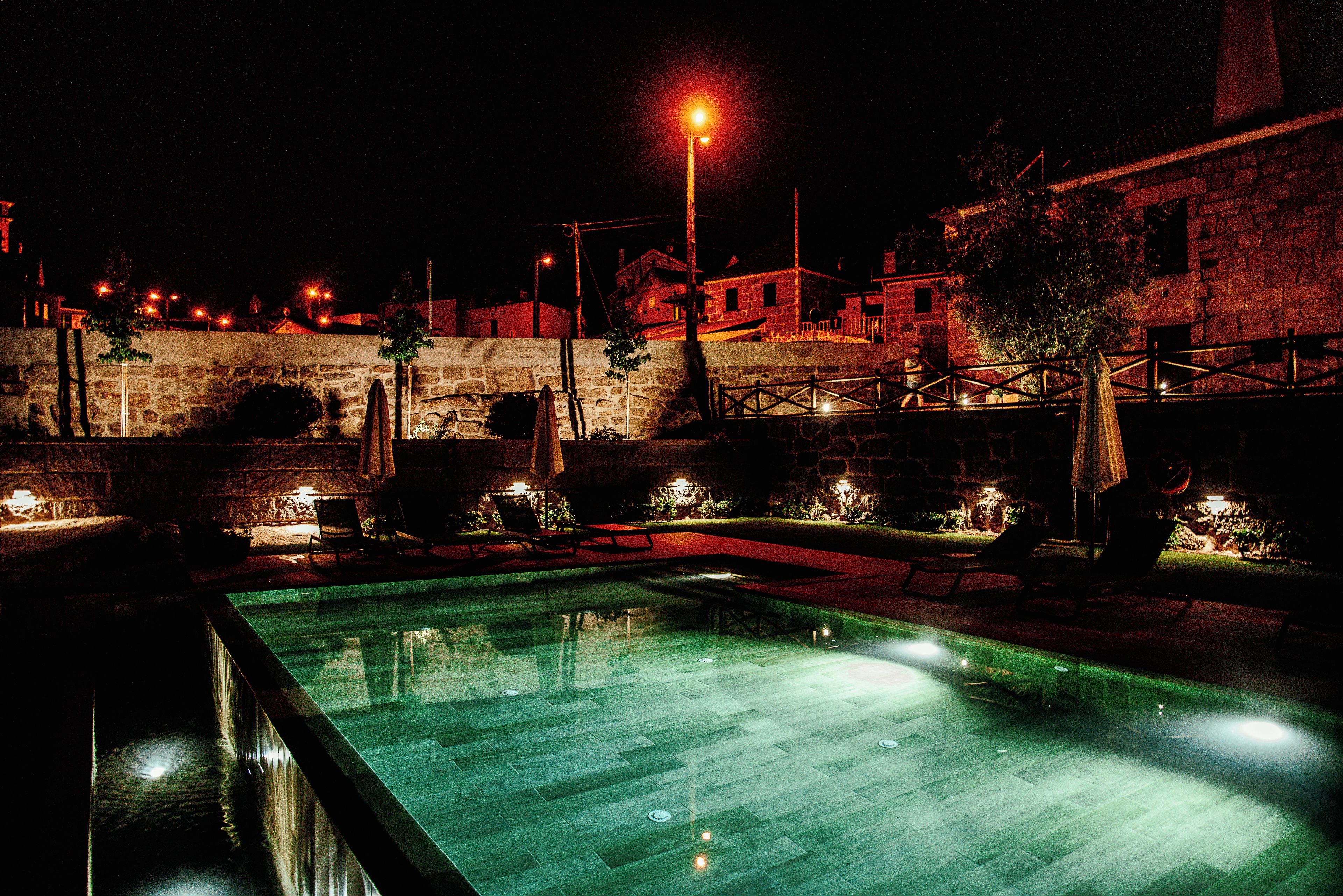 A nighttime view of a swimming pool with stone walls and outdoor seating.