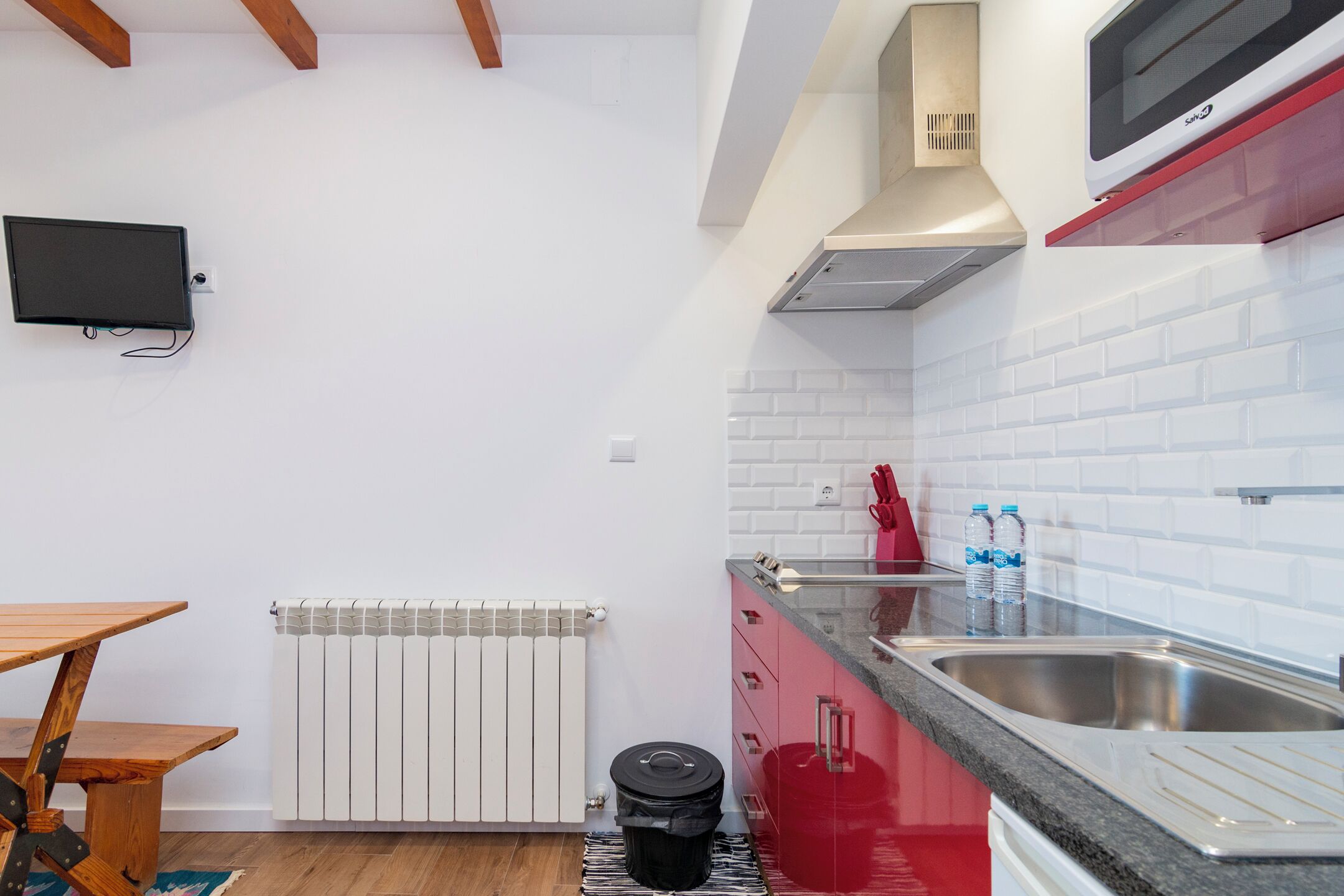Una cocina moderna con azulejos blancos tipo metro, encimera roja y pileta de acero inoxidable.