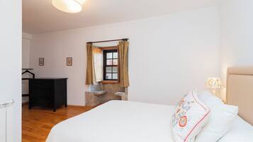 Ein Schlafzimmer mit einem Bett, einer Kommode, einem Fenster mit Vorhängen und einer Lampe.