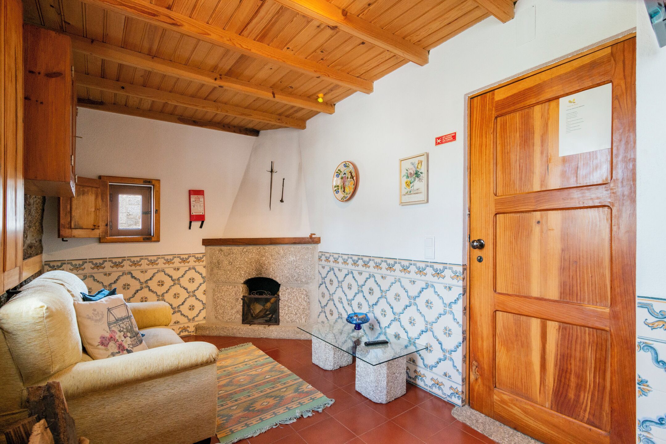Un salon chaleureux avec un plafond en bois, une cheminée, un canapé et un mur orné d’un motif.