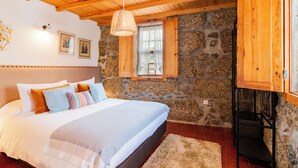 Un dormitorio con pared de piedra, techo de madera y una cama con muchos almohadones.