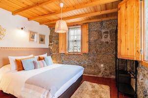 Un dormitorio con pared de piedra, techo de madera y una cama con muchos almohadones.