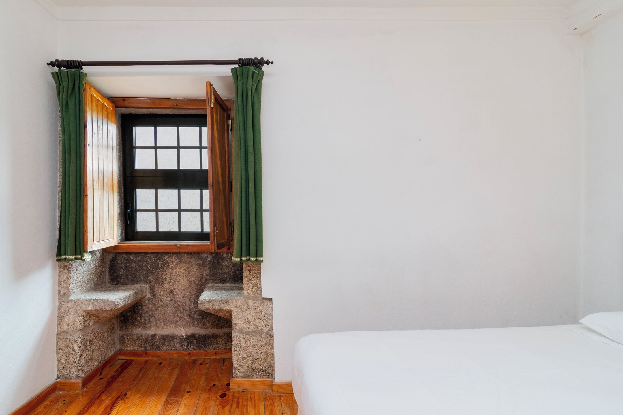 A room with a bed, a window with green curtains, and a stone staircase.