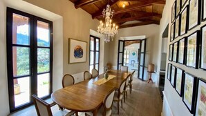 Una sala da pranzo con un grande tavolo in legno, sedie, un lampadario e quadri appesi alle pareti.