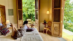 Una stanza con un letto, una sedia, un tavolo e vista su del verde all'esterno.