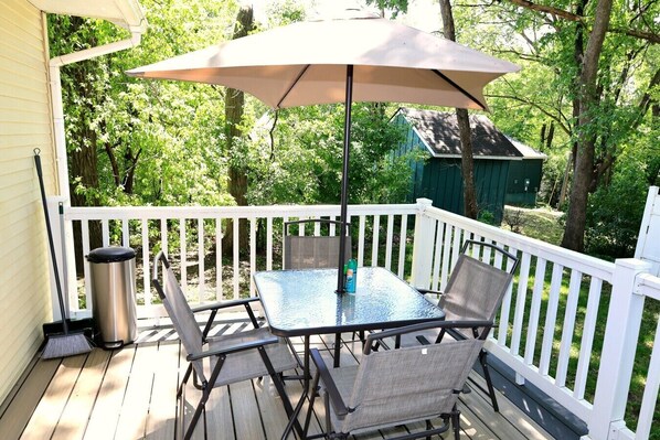 A covered outdoor deck with a table and chairs, a trash can, and a white railing. - Lake Life Meets City Vibes (Plymouth)