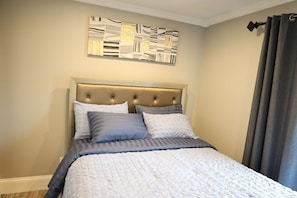 Une chambre à coucher avec une tête de lit capitonnée, un lit recouvert d’une courtepointe et une œuvre d’art murale au-dessus du lit.