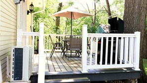 Una terraza de madera con mobiliario exterior, una parrilla y barandilla blanca.