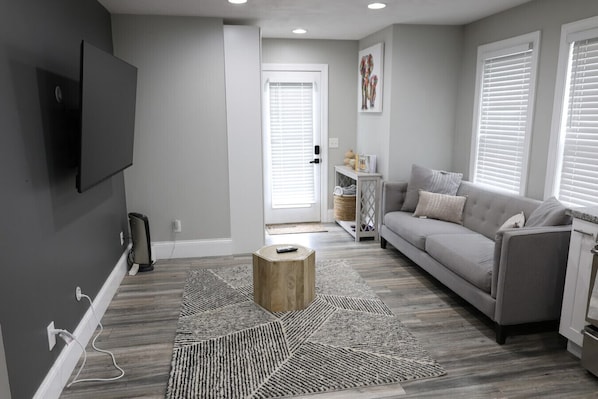 Un salon moderne avec un canapé gris, une table basse en bois et un téléviseur fixé au mur.