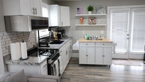 Una cocina moderna con armarios blancos, una estufa y un lavamanos. Hay una encimera con una cafetera y una cesta de objetos.